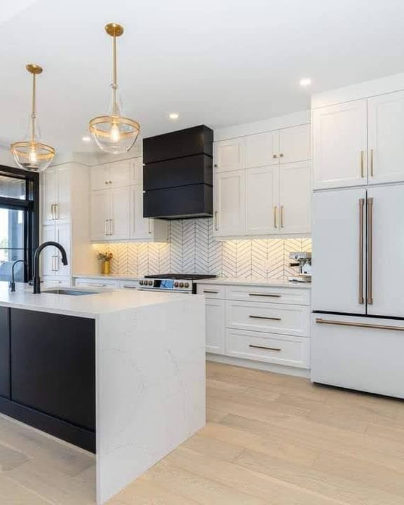 White shaker kitchen with a black waterfall quartz island, brass pendants and a black range hood, renovated by Elm Kitchen